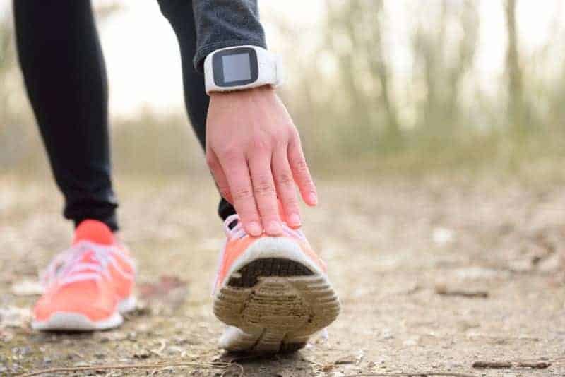 Runner stretching leg before run with smartwatch